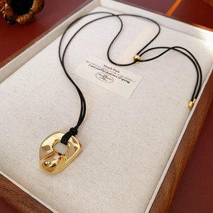 Macro shot of irregular golden pendant with black adjustable cord on a wooden tray