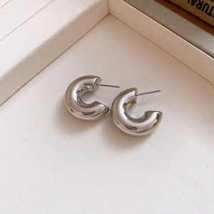 Detailed view of polished silver C-shaped chunky stud earrings on textured cream tray
