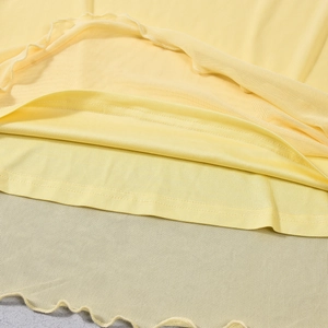 Detail of light yellow double-layer mini dress with mesh fabric and lettuce edge hemline