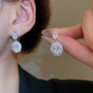 Detailed view of silver square earrings with clear zircon crystals on a person's hand