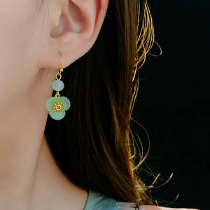 Detail of gold-plated flower drop earring with green translucent bead on a model