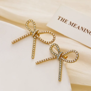 Detailed view of golden bow earrings featuring white pearls and sparkling crystals