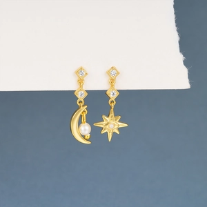Detail of asymmetric gold moon and star earrings featuring pearls and white zircons