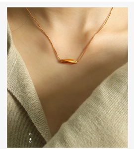 Detail showing high-polished gold twisted cylindrical pendant on a minimalist chain necklace