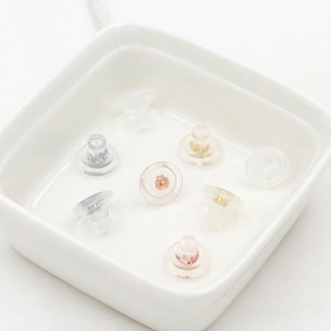 18K gold and clear silicone earring backs in various metal finishes on a ceramic tray