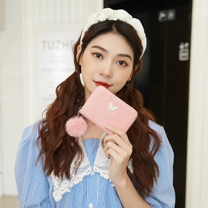 Pink zip-around lady wallet with butterfly logo and faux fur pompom charm held by hand
