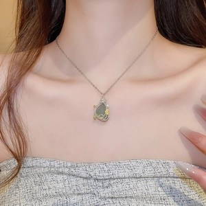 Detail of silver chain necklace with green stone pendant on female neck in natural light