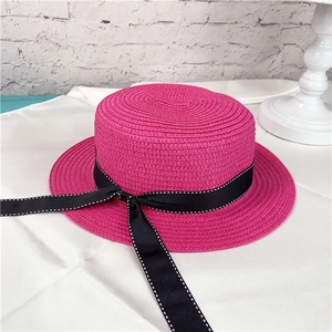 Detail of rose red straw boater hat featuring a black polka dot ribbon band trim