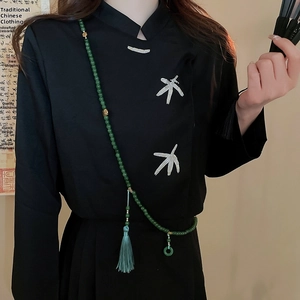 Détail d'un long collier de perles vertes avec pompons sur un haut noir brodé élégant