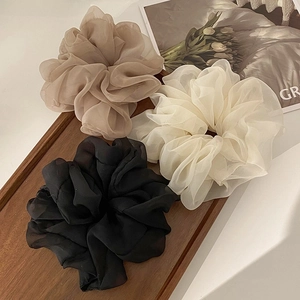 Three organza hair scrunchies in beige, white, and black displayed on a wooden tray