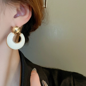 Detail of elegant gold metal ball earrings with white circular charms and polished trim