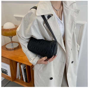 Detail of black pleated leather shoulder bag worn with a beige trench coat in a cozy room