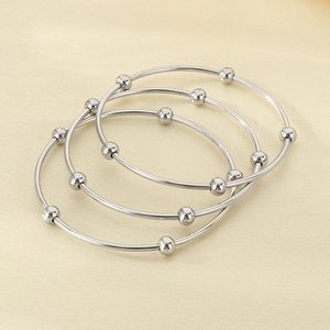 Macro detail of three silver titanium steel bangles with polished beads on fabric