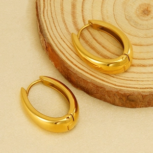 Boucles d'oreilles créoles ovales en acier doré poli sur fond bois chaleureux