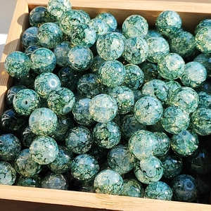 Detailed macro view of green marbled glass beads with gold accents in a wooden box
