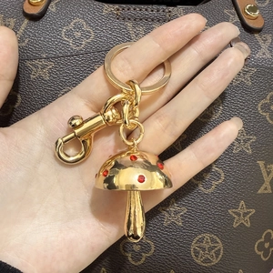 Close-up van gouden paddenstoel sleutelhanger met rode steentjes aan een handtas