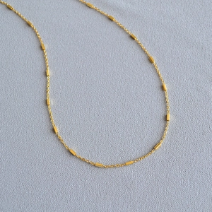 Detailed macro view of thin golden brass chain necklace with small cylindrical tube beads