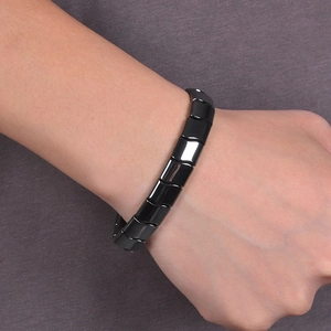 Close-up of a wide polished black magnetic hematite segment bracelet on a male wrist