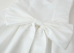Détail de la robe en satin blanc montrant le nœud élégant et l'éclat soyeux du tissu