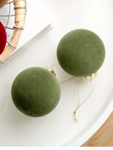 Detailed view of two moss green flocked Christmas balls with golden caps and strings