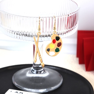 Close-up of asymmetric gold paintbrush and palette earrings on ribbed glass