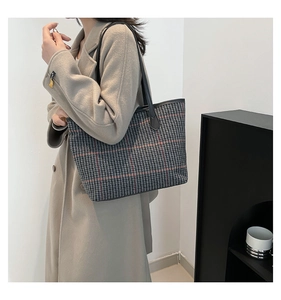 Detail of checkered tote bag with leather straps on model wearing a beige coat