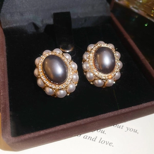 Close-up of vintage oval grey pearl earrings with sparkling rhinestones in a gold setting