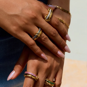 Close-up of stacked gold twist rings with colorful zircons and a MAMA charm bracelet
