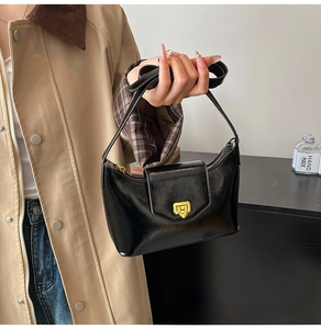 Detailed view of the shiny black underarm bag featuring a elegant gold metal lock and strap