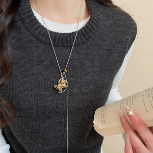 Gros plan détaillé d'un collier avec pendentif poney doré porté sur un pull gris