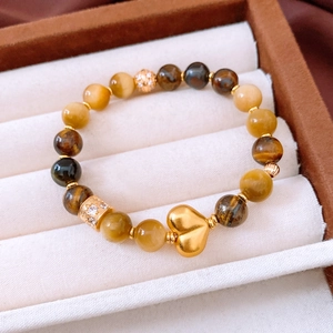 Dettaglio del ciondolo a cuore in oro 18k e delle perle occhio di tigre sul bracciale