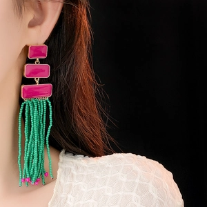 Close-up of long beaded tassel earrings with magenta enamel rectangles on female model