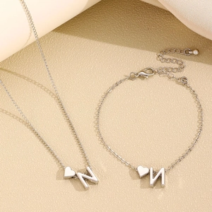 Détail des breloques cœur et lettre N en argent sur un ensemble collier et bracelet minimaliste