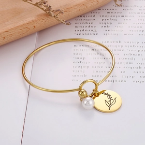 Detailansicht eines goldenen Geburtsblumen-Armbands mit Perlenanhänger und Blumengravur
