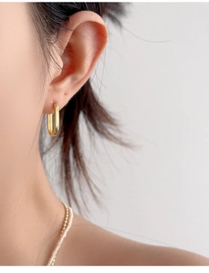 Close-up of elegant gold rectangular hoop earring on model with pearl necklace