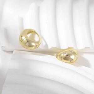 Detail of chunky gold hoop earrings with starburst zircon inlay on a textured white background