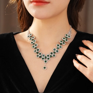 Close-up of floral pendant necklace with green gemstones and white diamonds on neck