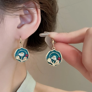Close-up of blue-green enamel flower earrings with pearl accents and golden metal finish