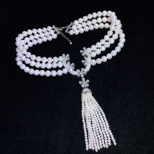 Detailed close-up of three-layer pearl necklace with floral pendant and tassel on black background
