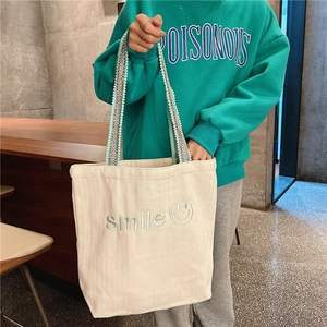Detail of canvas tote featuring blue smile embroidery and geometric woven tassel strap