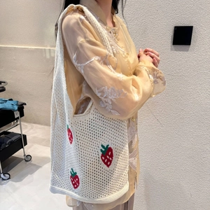 Detail of white crochet tote bag featuring red strawberry embroidery worn by a model