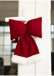 Detail of red velvet Christmas bow with white faux fur trim hanging on a white door handle