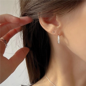 Detail of silver hoop earrings and ball studs worn by a model in a natural setting