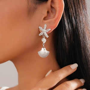 Detailed close-up of starfish and seashell charms on asymmetric silver drop earrings