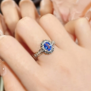 Close-up of a 3-carat oval blue sapphire ring with a sparkling halo on a model's hand