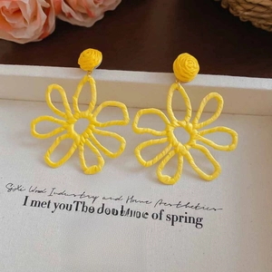 Detailed view of yellow woven flower earrings with hollow petals on an elegant white base