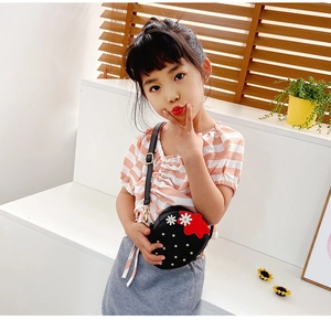 Girl wearing strawberry-shaped black crossbody bag with red leaf and white flower detail