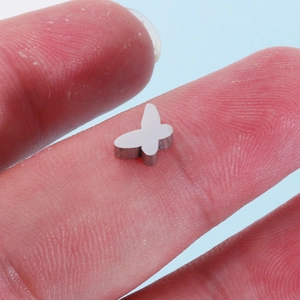 Polished silver butterfly stainless steel charm displayed on a fingertip for size