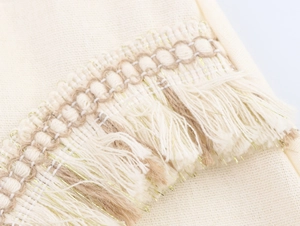 Macro detail of beige woven fabric with intricate fringe tassels and gold metallic thread