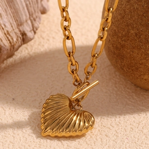 Detail of 18K gold plated heart pendant necklace with toggle clasp on a textured surface